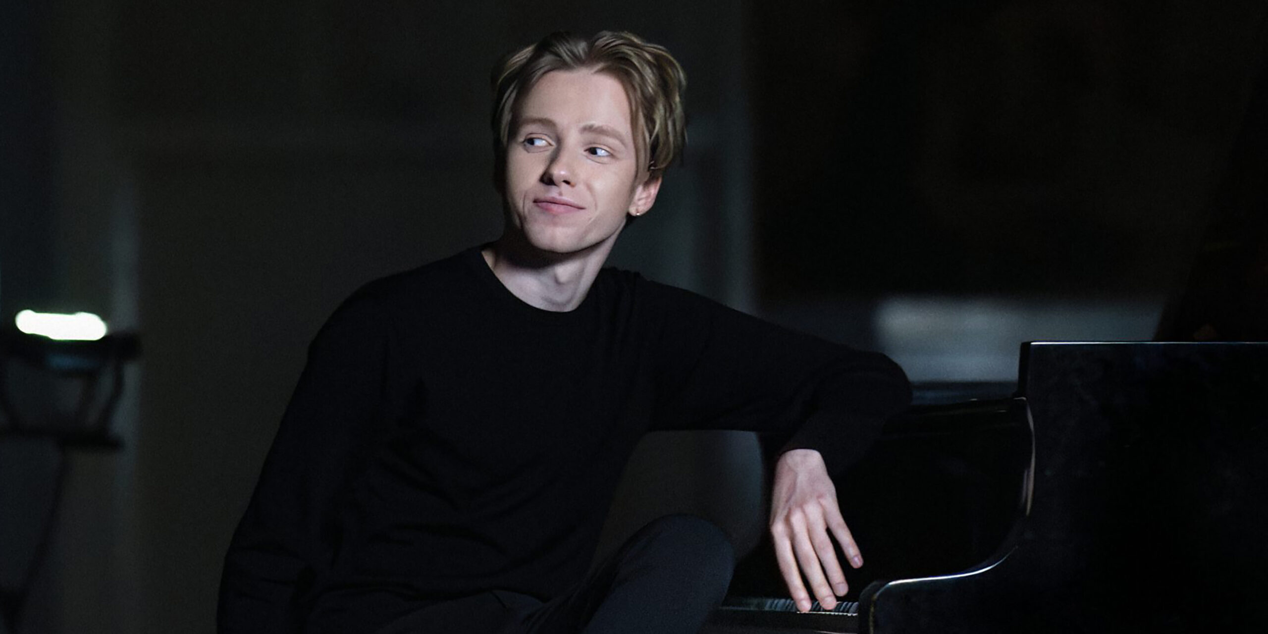 White man sits at a piano and looks to the side.