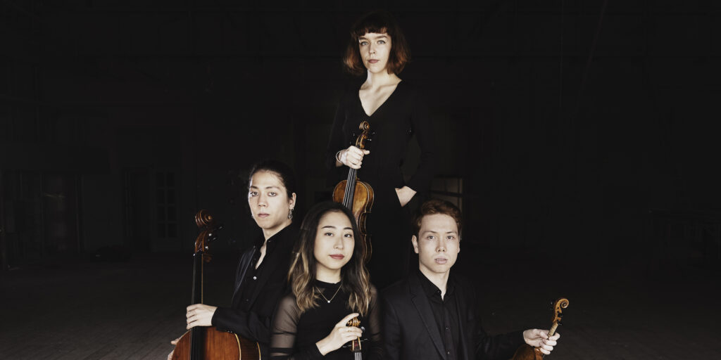 two men and two women pose with stringed instruments in front of a black backdrop