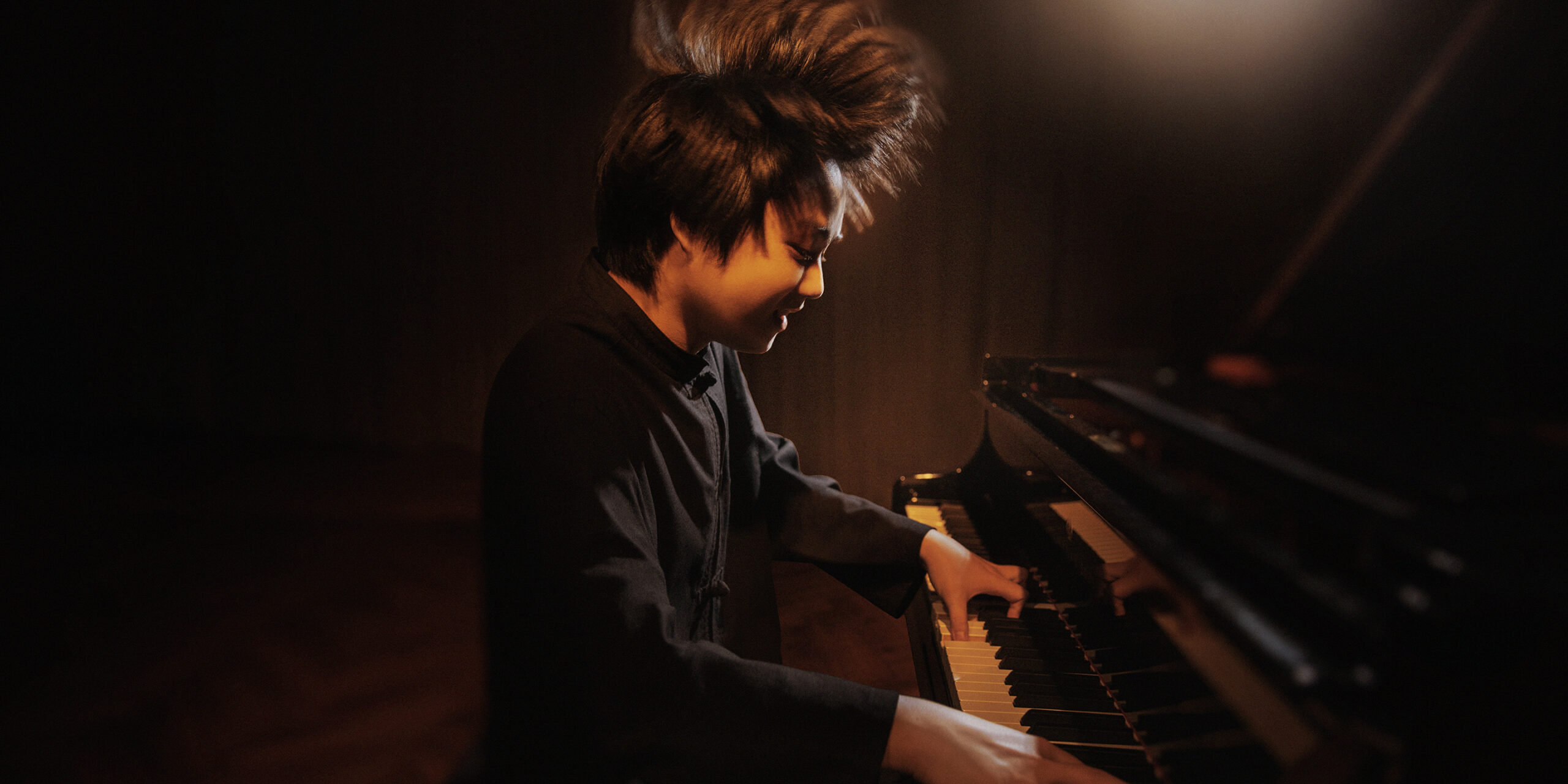 Asian man playing the piano enthusiastically, with his hair standing on end.